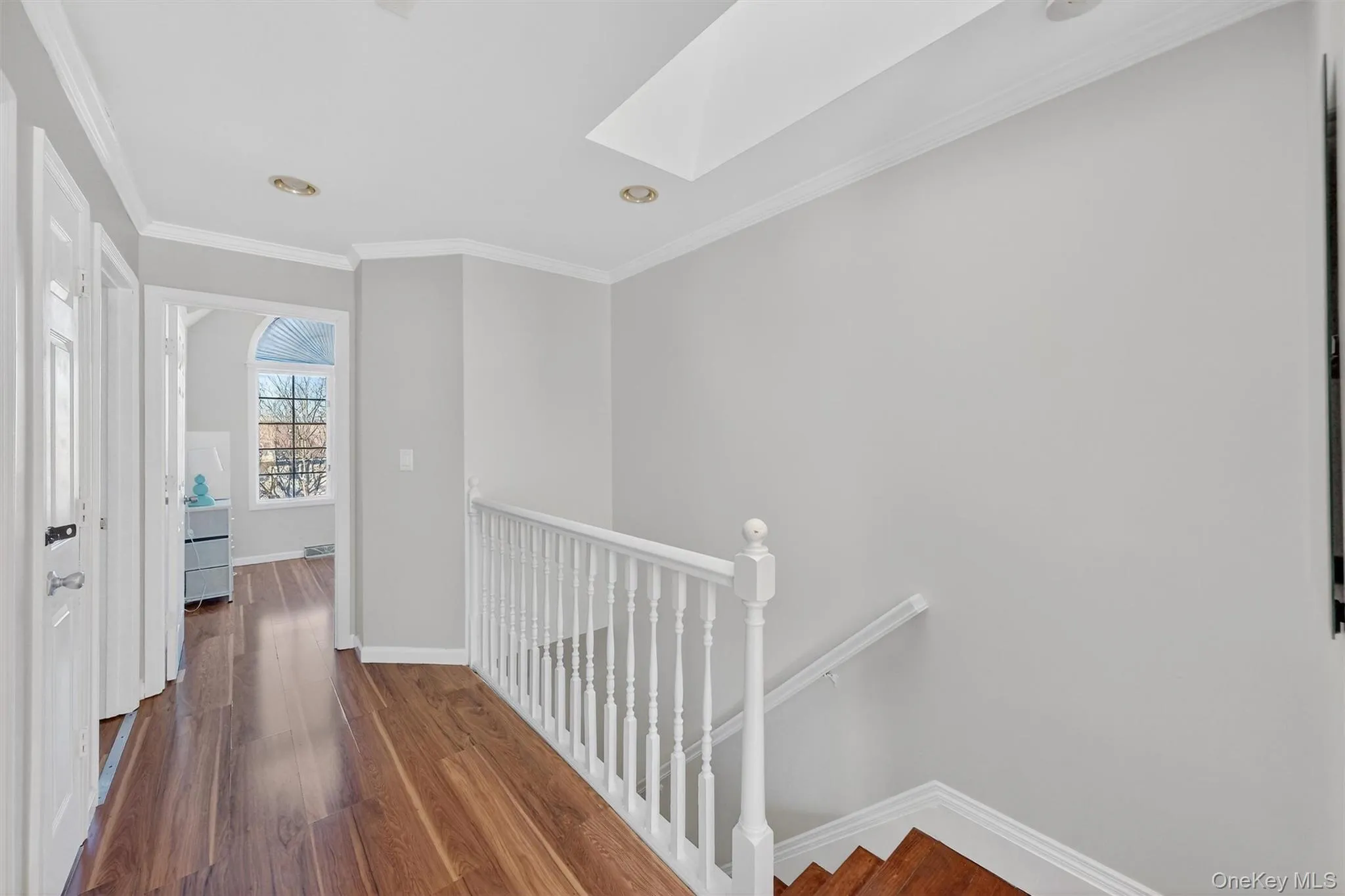 Hall featuring an upstairs landing, a skylight, dark wood-style flooring, and crown molding Hall featuring an upstairs landing, a skylight, dark wood-style flooring, and crown molding
