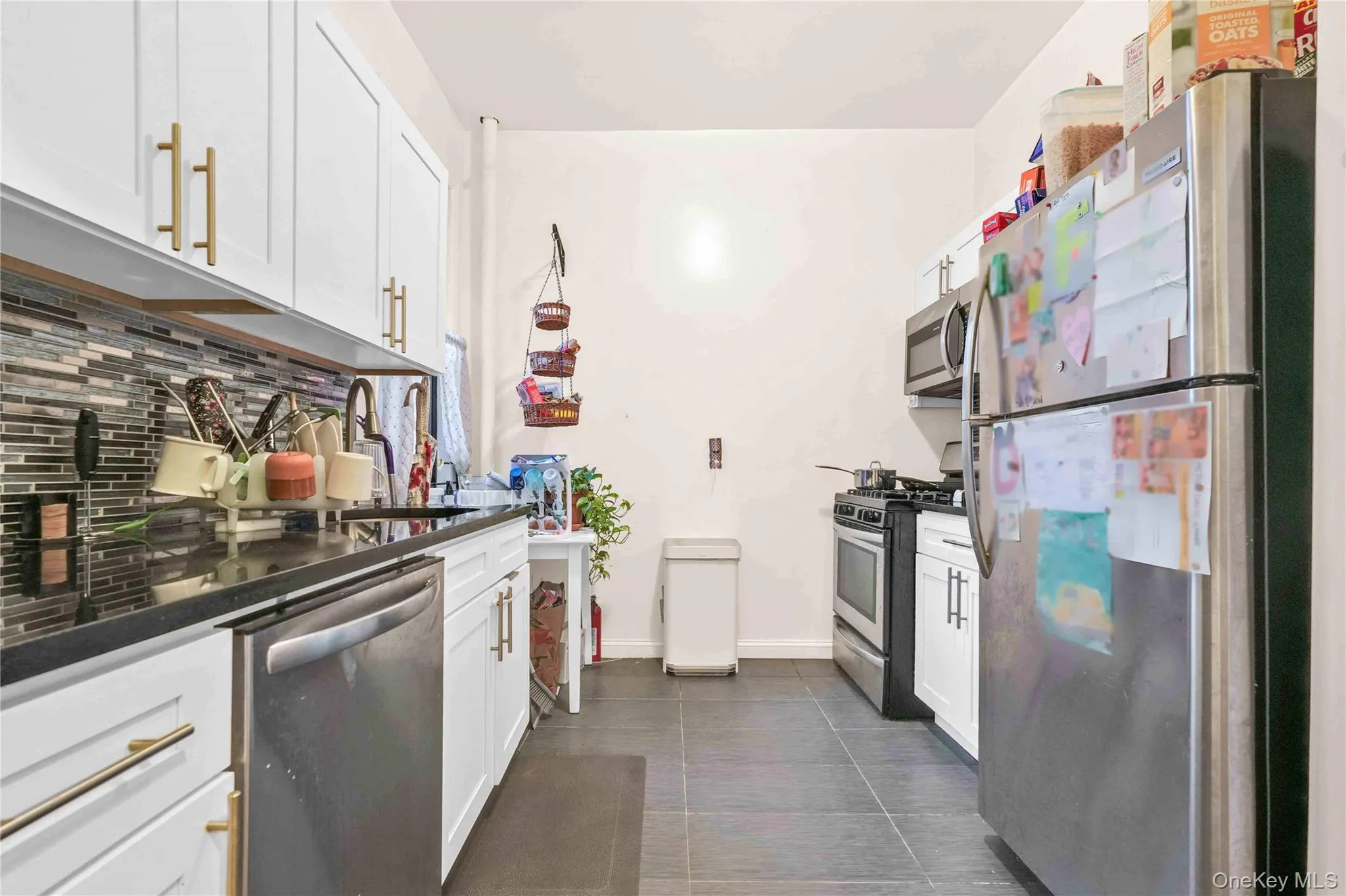 Kitchen featuring appliances with stainless steel finishes, white cabinetry, dark tile patterned flooring, decorative backsplash, and dark stone countertops Kitchen featuring appliances with stainless steel finishes, white cabinetry, dark tile patterned flooring, decorative backsplash, and dark stone countertops