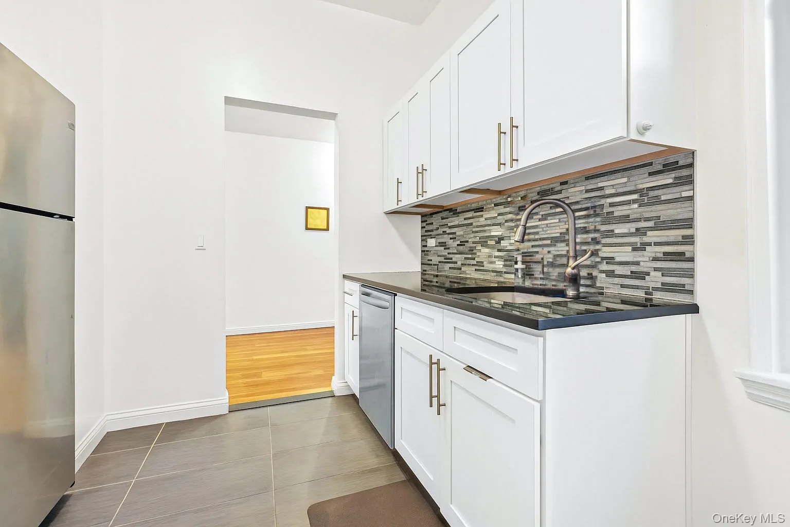 Kitchen featuring appliances with stainless steel finishes, light tile patterned floors, white cabinets, decorative backsplash, and dark stone counters Kitchen featuring appliances with stainless steel finishes, light tile patterned floors, white cabinets, decorative backsplash, and dark stone counters