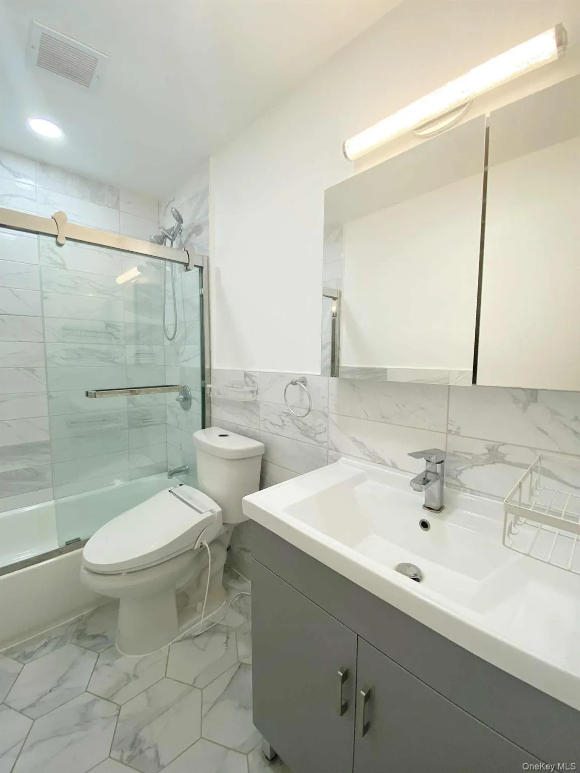 Bathroom with tile walls, vanity, wainscoting, light marble finish floors, and bath / shower combo with glass door Bathroom with tile walls, vanity, wainscoting, light marble finish floors, and bath / shower combo with glass door