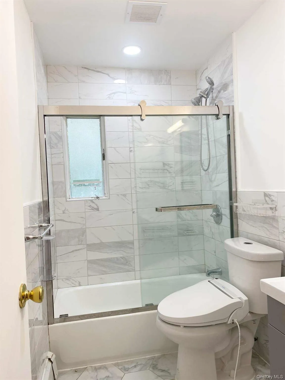 Bathroom featuring vanity, marble finish flooring, tile walls, shower / bath combination with glass door, and baseboard heating Bathroom featuring vanity, marble finish flooring, tile walls, shower / bath combination with glass door, and baseboard heating