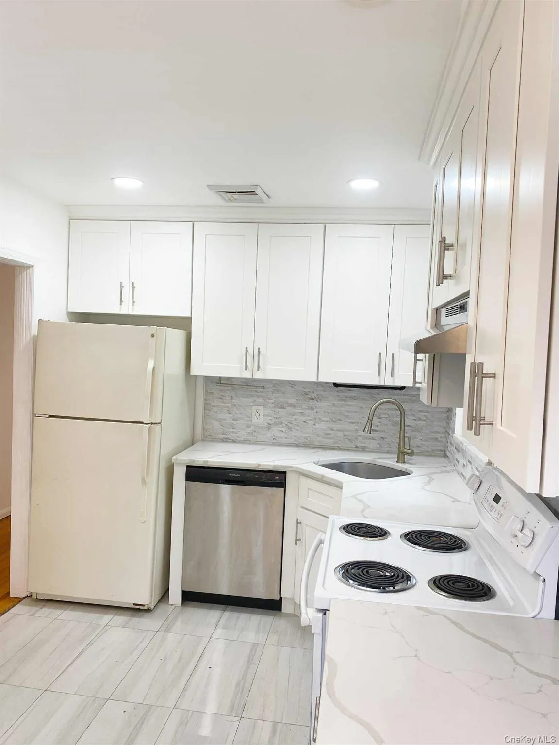 Kitchen with white appliances, white cabinetry, tasteful backsplash, light stone countertops, and under cabinet range hood Kitchen with white appliances, white cabinetry, tasteful backsplash, light stone countertops, and under cabinet range hood