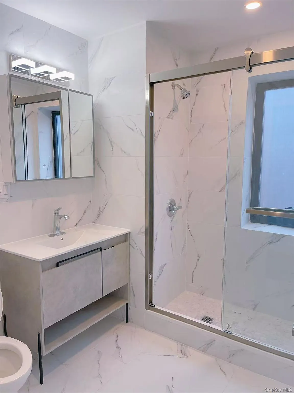Bathroom featuring marble finish flooring, a marble finish shower, tile walls, and vanity Bathroom featuring marble finish flooring, a marble finish shower, tile walls, and vanity