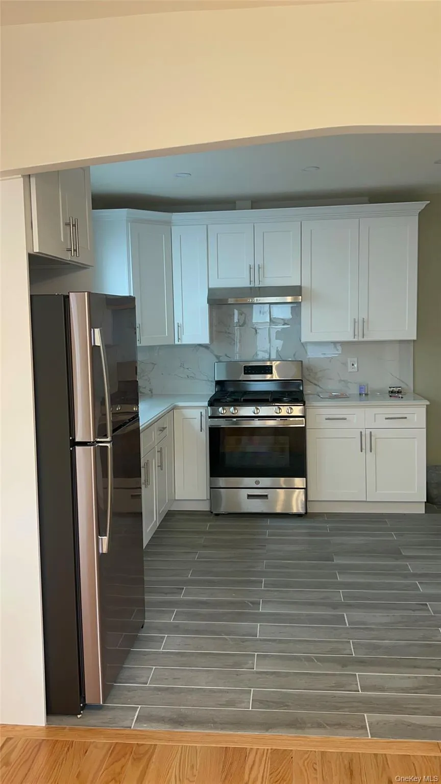 Kitchen featuring stainless steel appliances, white cabinets, tasteful backsplash, wood tiled floors, and under cabinet range hood Kitchen featuring stainless steel appliances, white cabinets, tasteful backsplash, wood tiled floors, and under cabinet range hood