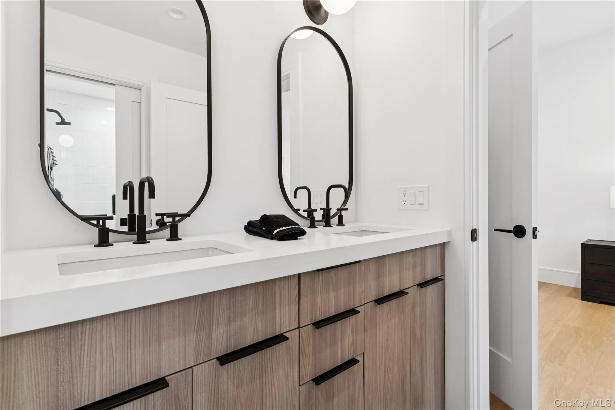 Full guest bath with double vanity, light wood-style flooring, and a tile shower Full guest bath with double vanity, light wood-style flooring, and a tile shower