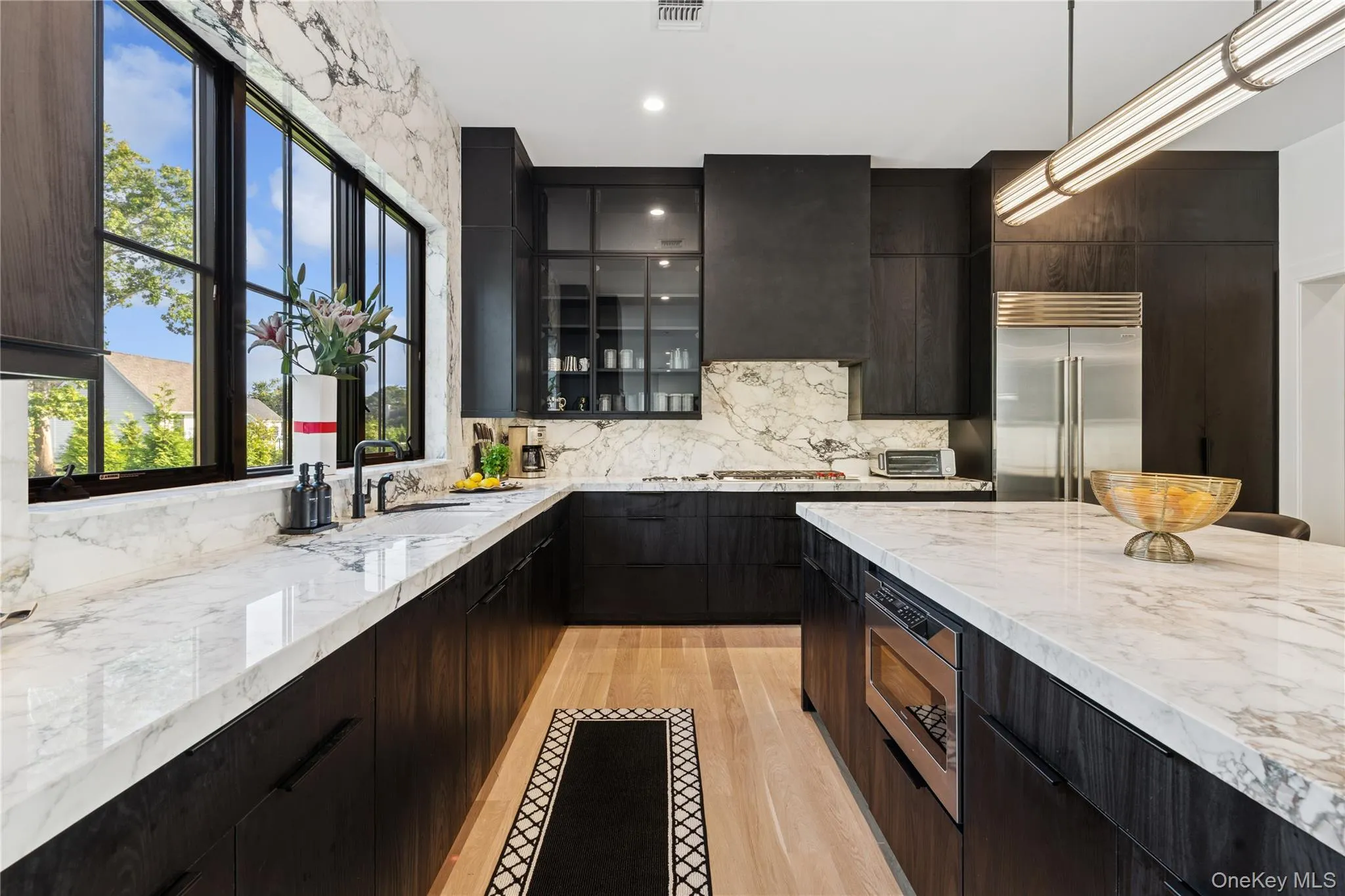 Kitchen featuring recessed lighting, light wood-type flooring, modern cabinets, built in appliances, and light stone countertops Kitchen featuring recessed lighting, light wood-type flooring, modern cabinets, built in appliances, and light stone countertops