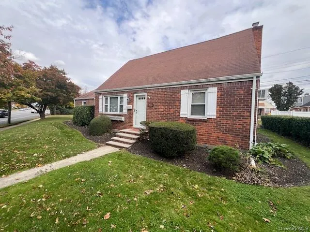 Cape cod house featuring a front yard, brick siding, and a chimney Cape cod house featuring a front yard, brick siding, and a chimney