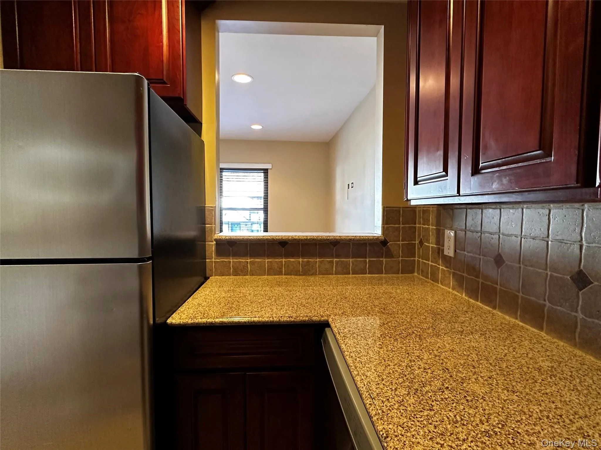 Kitchen with freestanding refrigerator, decorative backsplash, light stone counters, recessed lighting, and cherry wood cabinets Kitchen with freestanding refrigerator, decorative backsplash, light stone counters, recessed lighting, and cherry wood cabinets