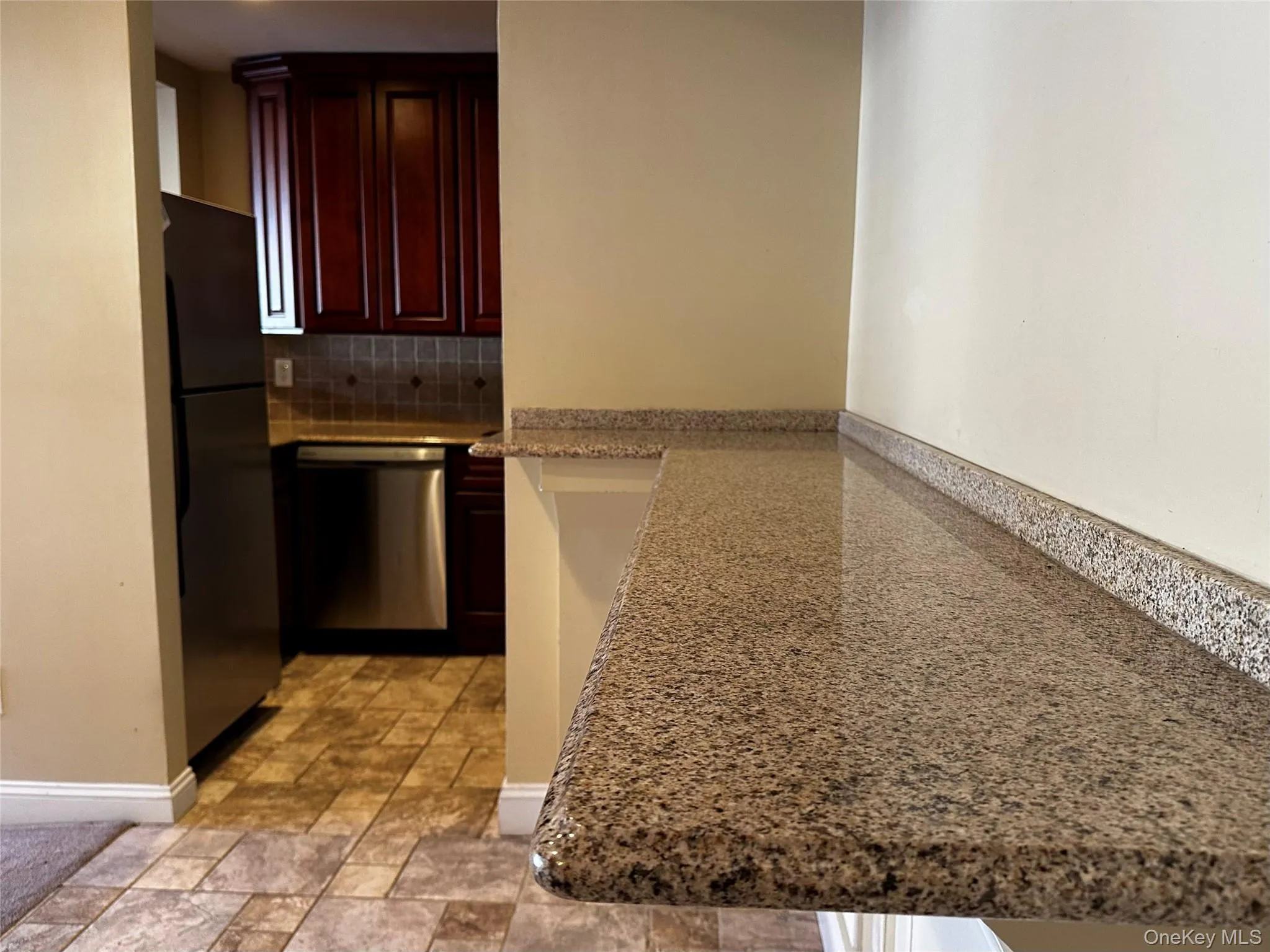 Kitchen with backsplash, stainless steel dishwasher, freestanding refrigerator, light stone countertops, and a breakfast bar. Kitchen with backsplash, stainless steel dishwasher, freestanding refrigerator, light stone countertops, and a breakfast bar.