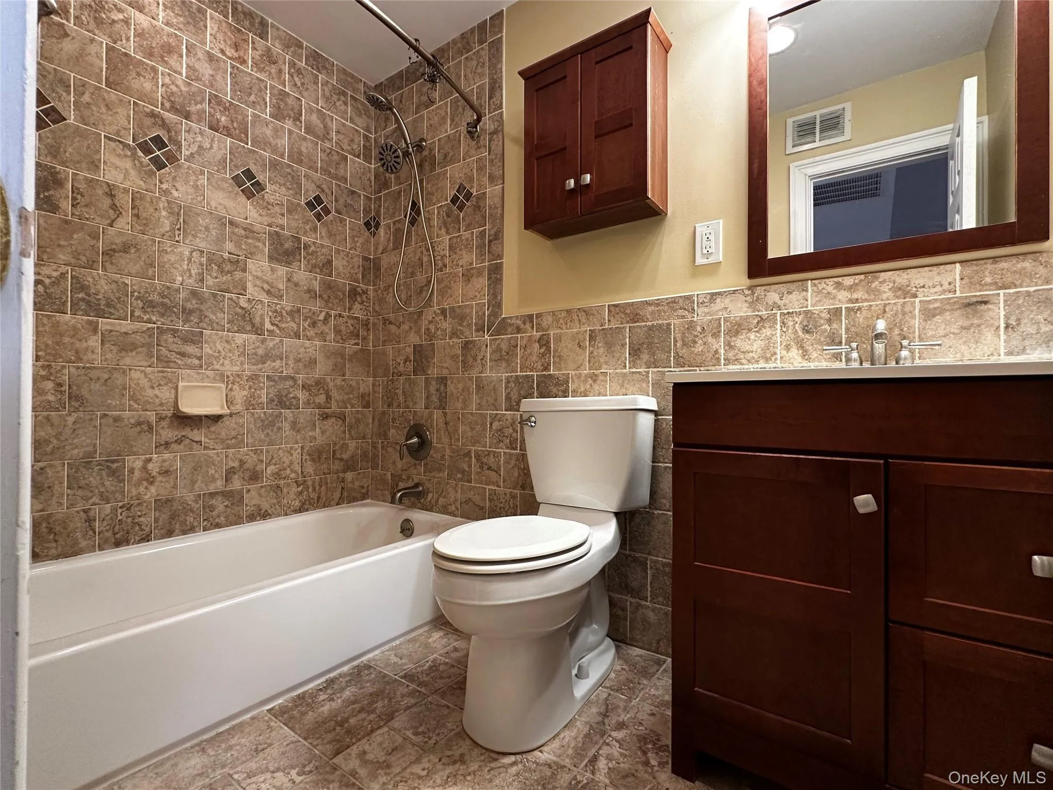 Full bath featuring tile walls, vanity, shower / tub combination, and wainscoting Full bath featuring tile walls, vanity, shower / tub combination, and wainscoting