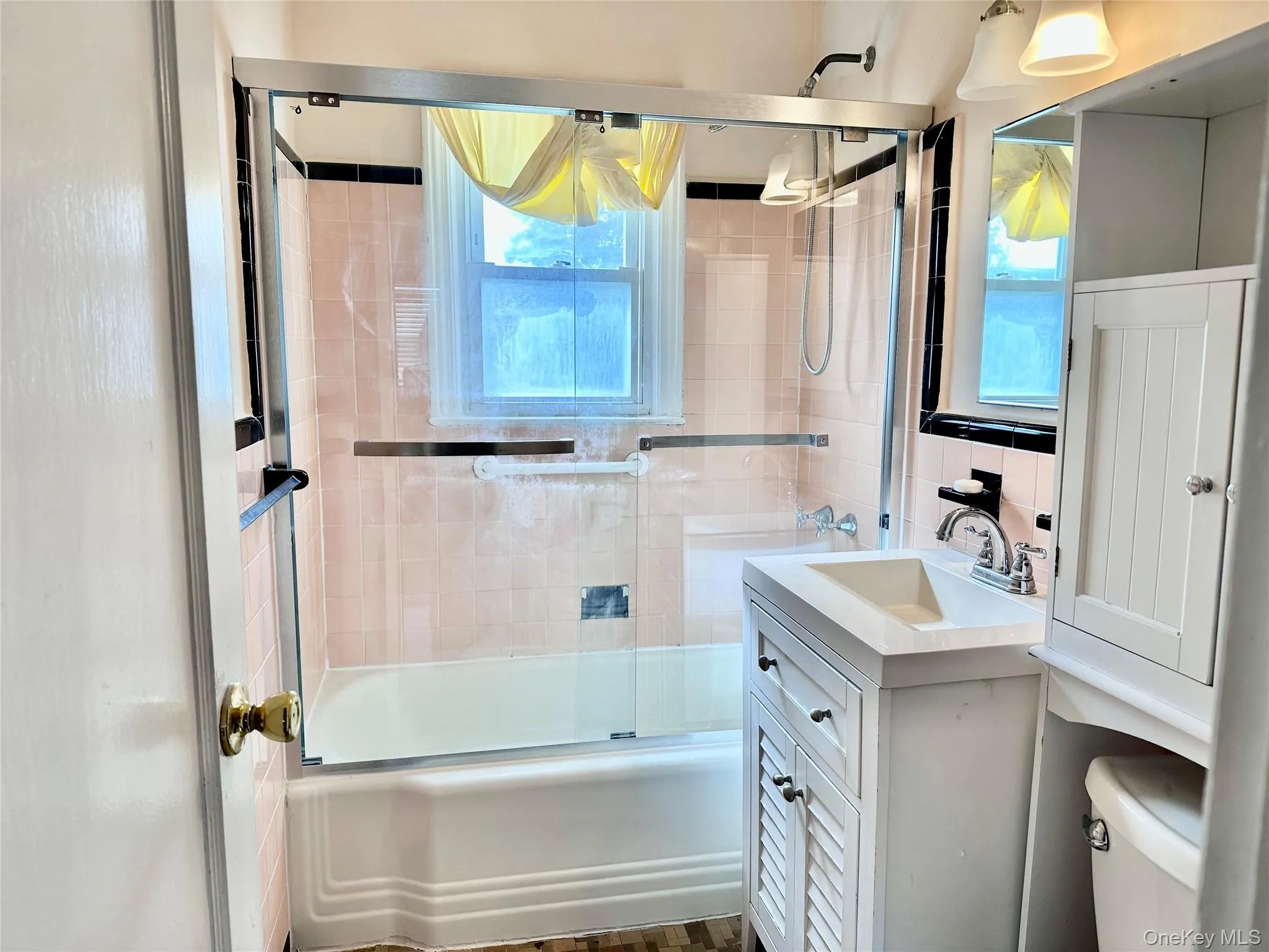 Full bathroom featuring shower / bath combination with glass door, healthy amount of natural light, vanity, and tile walls Full bathroom featuring shower / bath combination with glass door, healthy amount of natural light, vanity, and tile walls