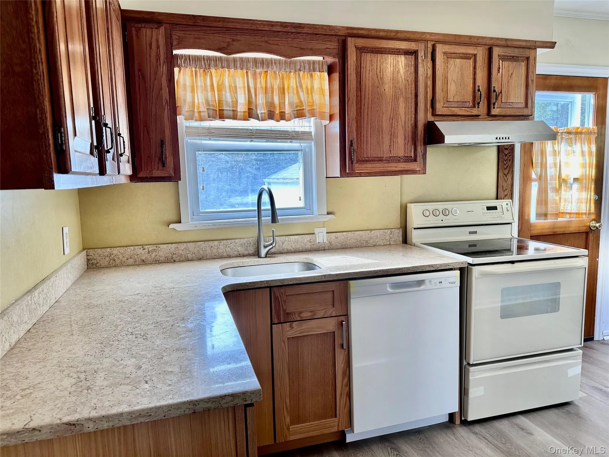 Kitchen featuring white appliances, plenty of natural light, light stone countertops, and extractor fan Kitchen featuring white appliances, plenty of natural light, light stone countertops, and extractor fan