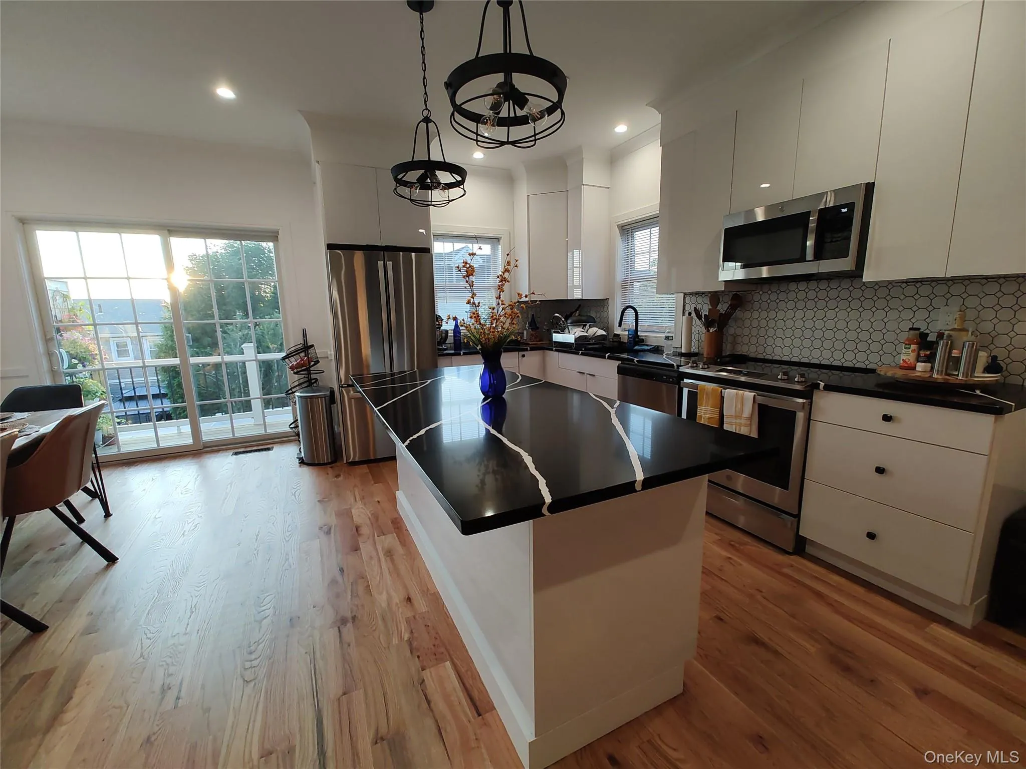 Kitchen with a center island, stainless steel appliances, tasteful backsplash, light wood-style floors, and white cabinets Kitchen with a center island, stainless steel appliances, tasteful backsplash, light wood-style floors, and white cabinets