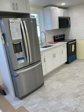 Kitchen featuring stainless steel fridge with ice dispenser, range with electric stovetop, white cabinetry, light countertops, and backsplash Kitchen featuring stainless steel fridge with ice dispenser, range with electric stovetop, white cabinetry, light countertops, and backsplash