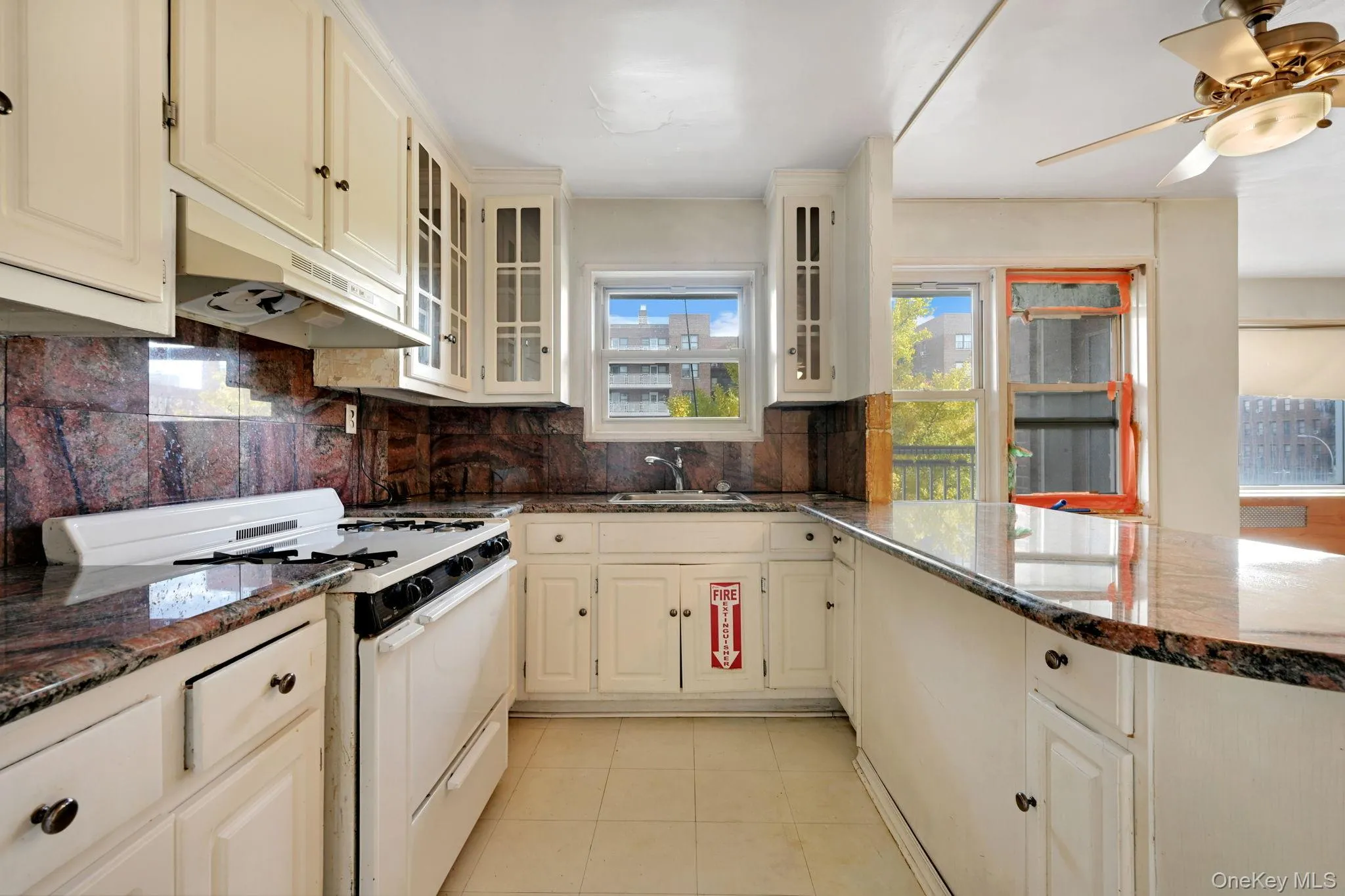 Kitchen with white gas range, dark stone counters, decorative backsplash, under cabinet range hood, and cream cabinets Kitchen with white gas range, dark stone counters, decorative backsplash, under cabinet range hood, and cream cabinets