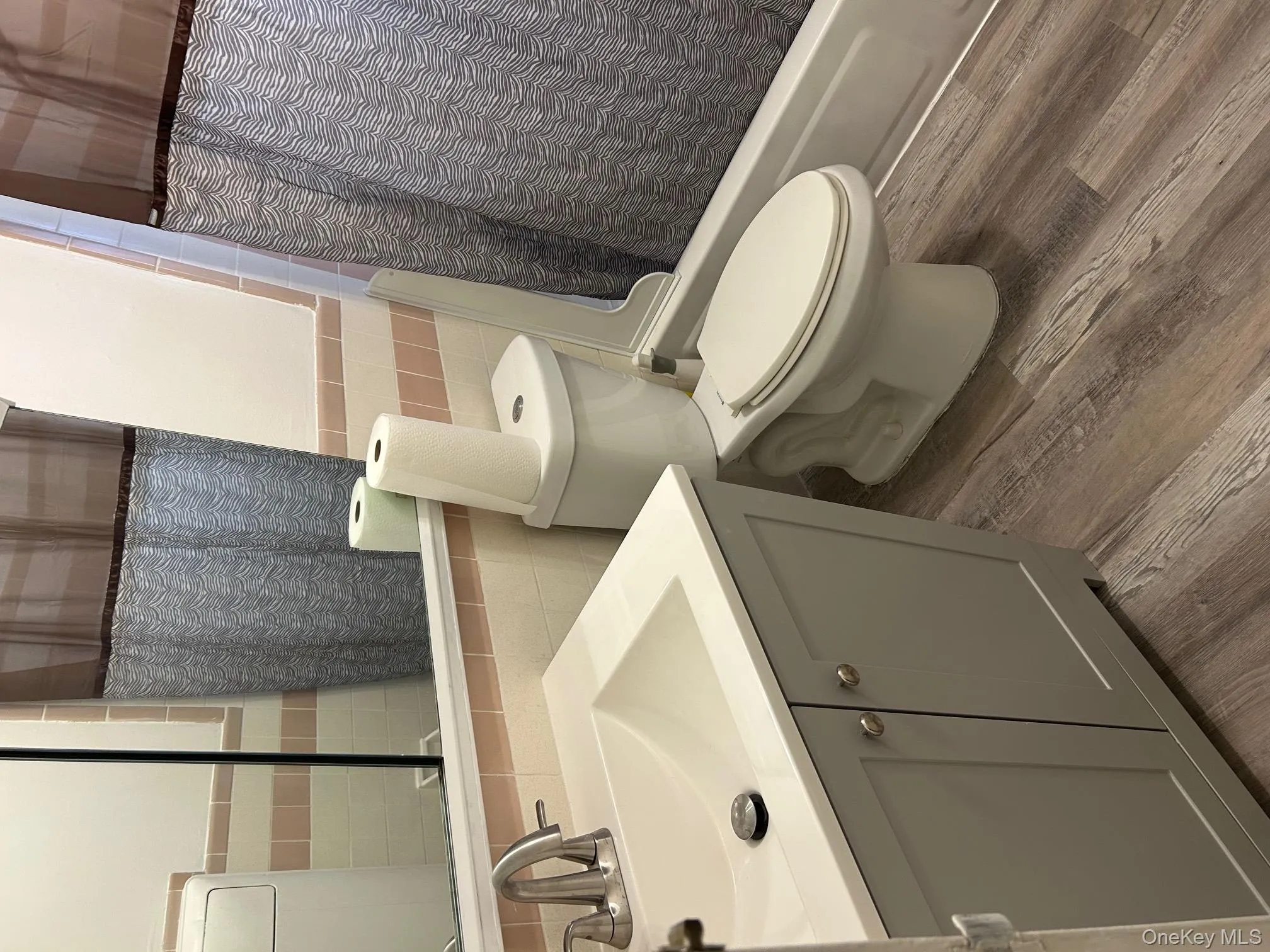 Bathroom featuring tile walls, shower / bath combination with curtain, vanity, wood finished floors, and wainscoting Bathroom featuring tile walls, shower / bath combination with curtain, vanity, wood finished floors, and wainscoting