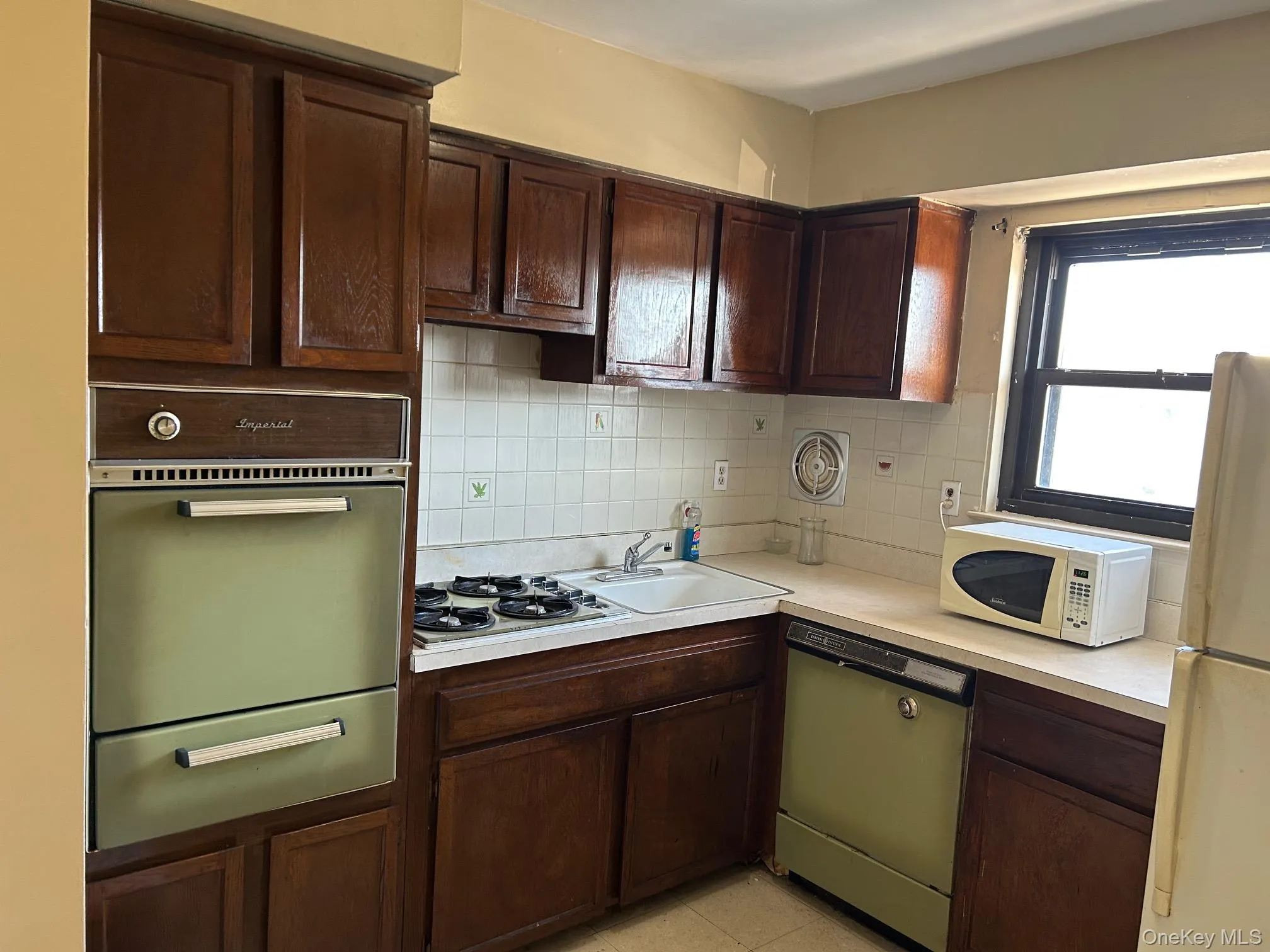 Kitchen with dark brown cabinets, white appliances, light countertops, a warming drawer, and decorative backsplash Kitchen with dark brown cabinets, white appliances, light countertops, a warming drawer, and decorative backsplash