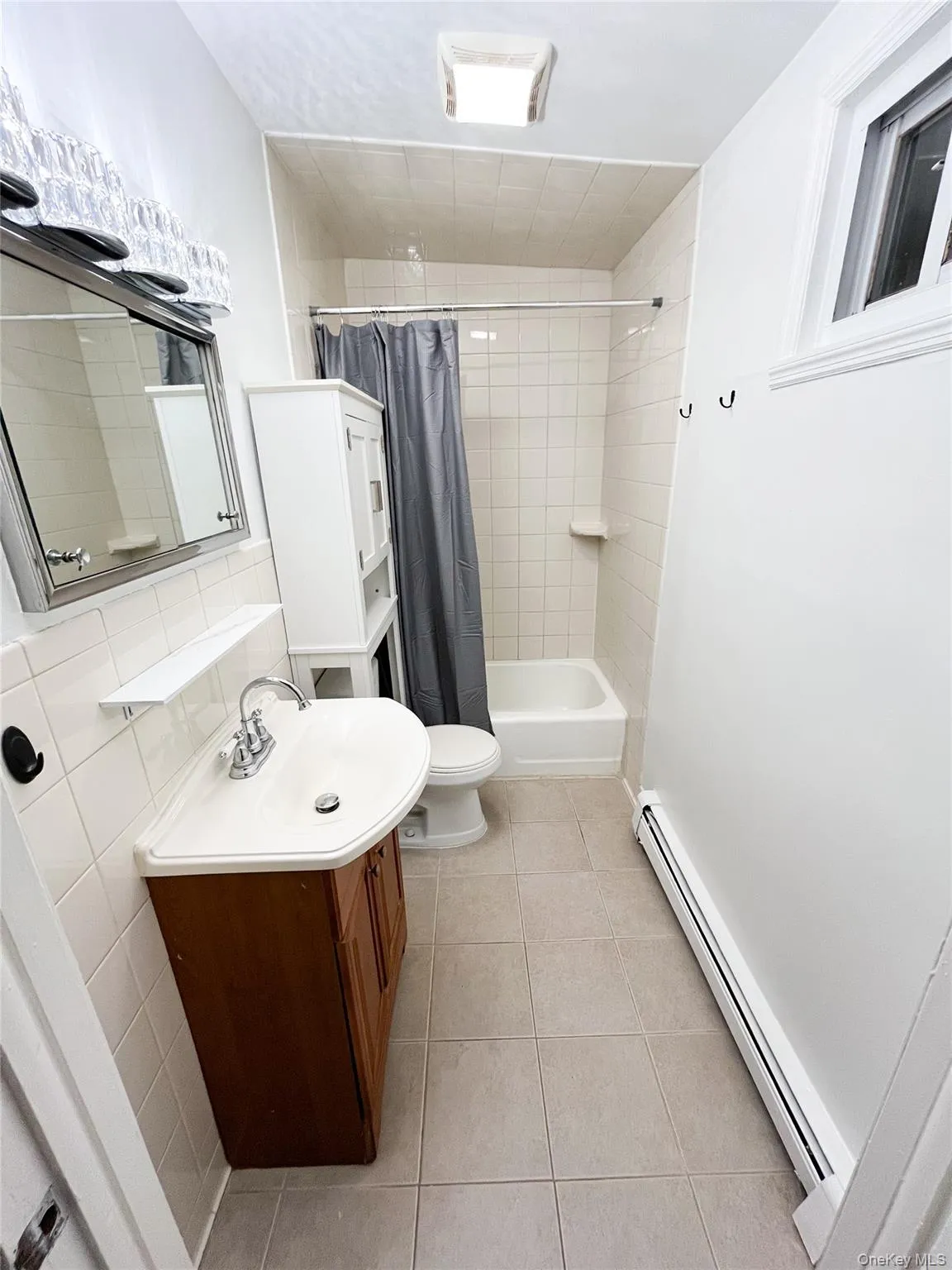 Bathroom with a baseboard heating unit, vanity, light tile patterned flooring, and shower / bath combo with shower curtain Bathroom with a baseboard heating unit, vanity, light tile patterned flooring, and shower / bath combo with shower curtain