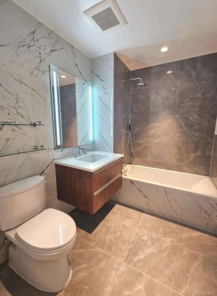 Bathroom featuring vanity, tile walls, a combined bath / shower with marble appearance, and recessed lighting Bathroom featuring vanity, tile walls, a combined bath / shower with marble appearance, and recessed lighting