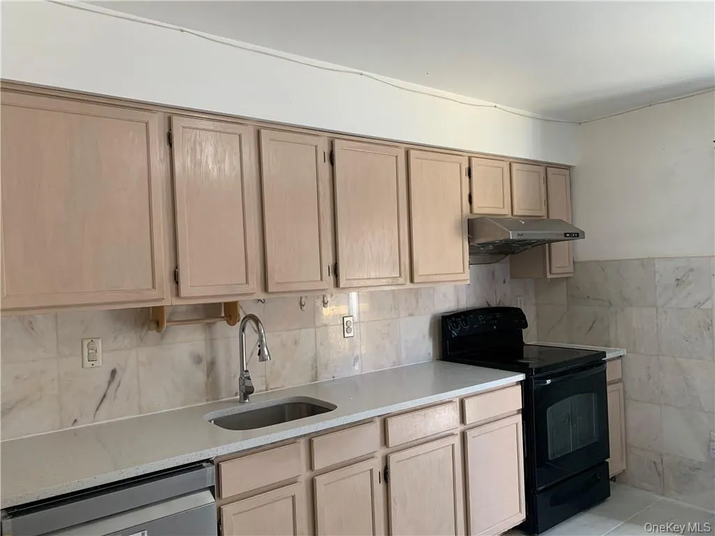 Kitchen with dishwasher, black range with electric cooktop, sink, light tile patterned floors, and light brown cabinetry Kitchen with dishwasher, black range with electric cooktop, sink, light tile patterned floors, and light brown cabinetry