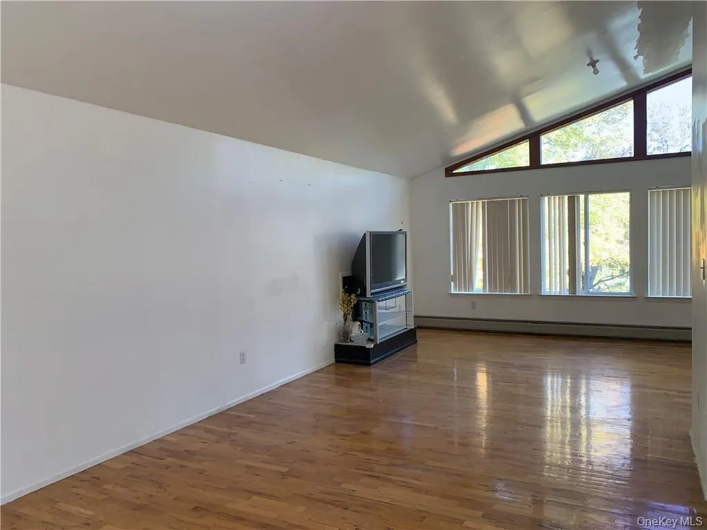 Unfurnished living room featuring lofted ceiling, hardwood / wood-style floors, and a baseboard radiator Unfurnished living room featuring lofted ceiling, hardwood / wood-style floors, and a baseboard radiator