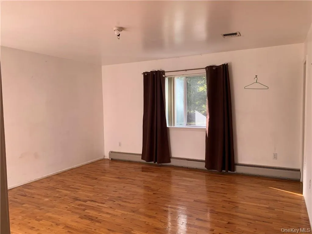 Unfurnished room with hardwood / wood-style flooring and a baseboard radiator Unfurnished room with hardwood / wood-style flooring and a baseboard radiator