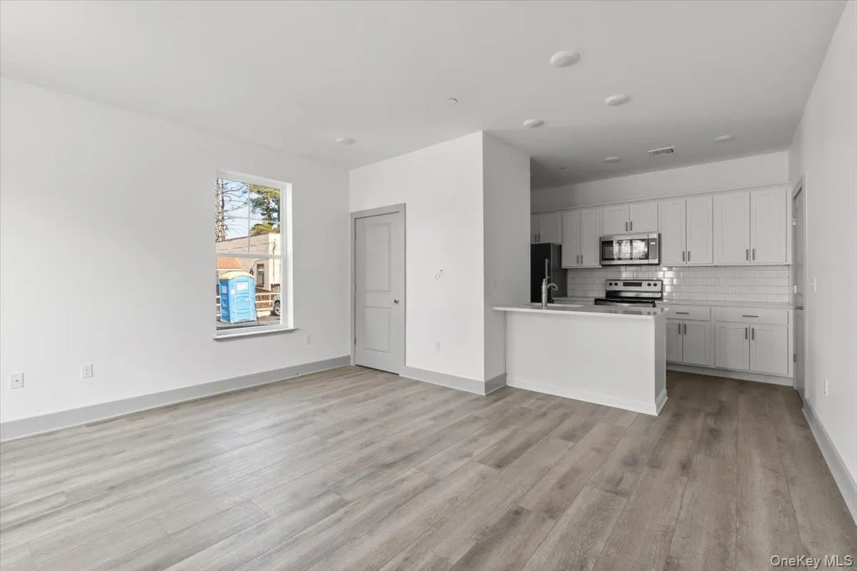 Kitchen featuring open floor plan, tasteful backsplash, appliances with stainless steel finishes, white cabinets, and light wood-style flooring Kitchen featuring open floor plan, tasteful backsplash, appliances with stainless steel finishes, white cabinets, and light wood-style flooring