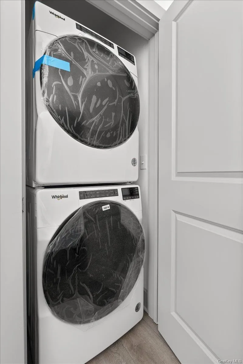 Washroom featuring wood finished floors and stacked washing machine and dryer Washroom featuring wood finished floors and stacked washing machine and dryer