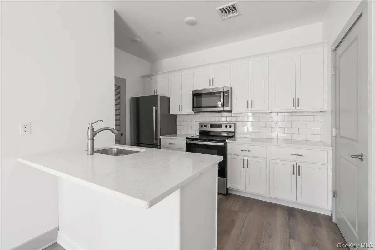 Kitchen with stainless steel appliances, white cabinetry, light stone countertops, decorative backsplash, and a peninsula Kitchen with stainless steel appliances, white cabinetry, light stone countertops, decorative backsplash, and a peninsula