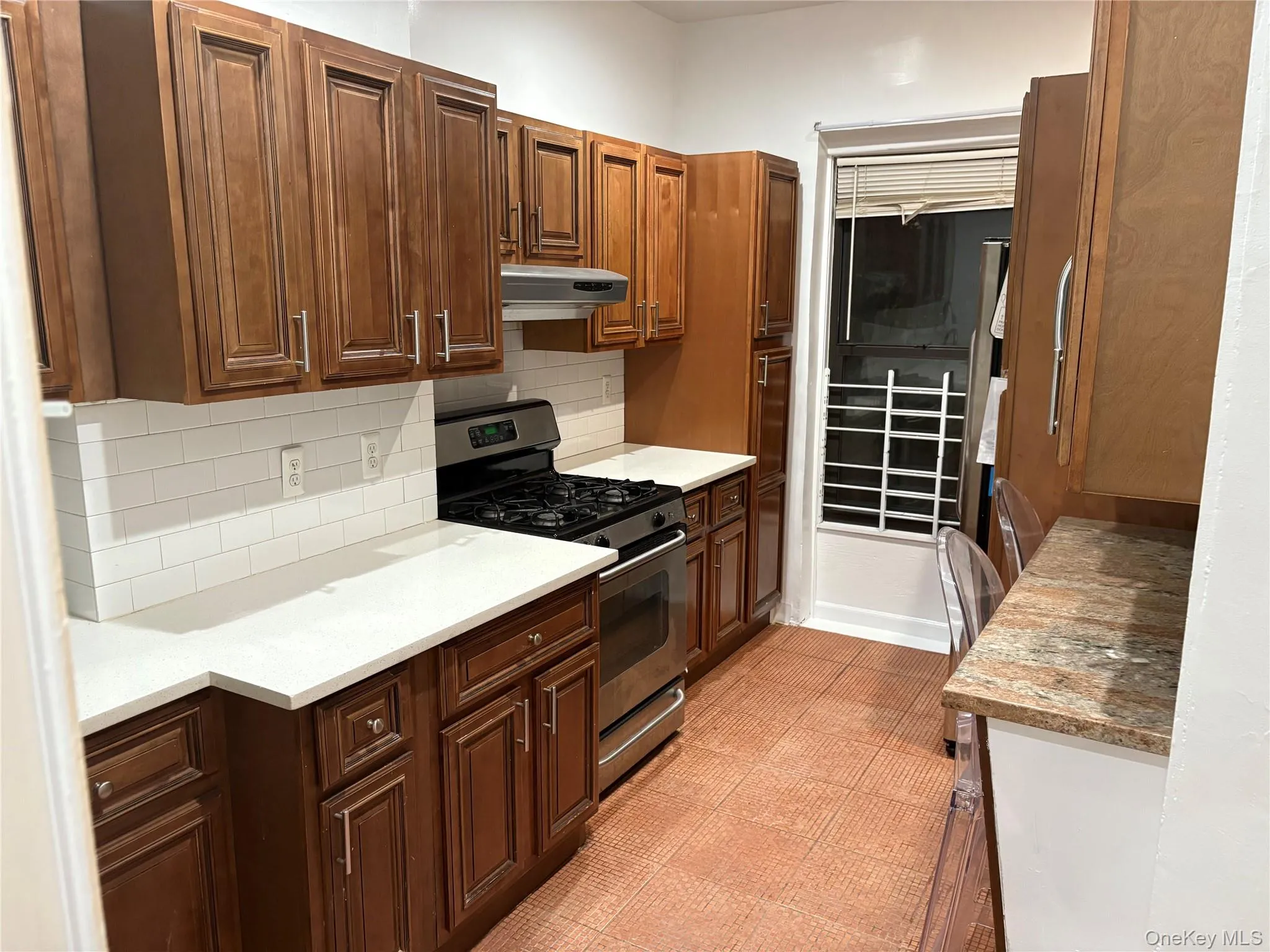 Kitchen with stainless steel gas range oven, decorative backsplash, light stone countertops, and under cabinet range hood Kitchen with stainless steel gas range oven, decorative backsplash, light stone countertops, and under cabinet range hood