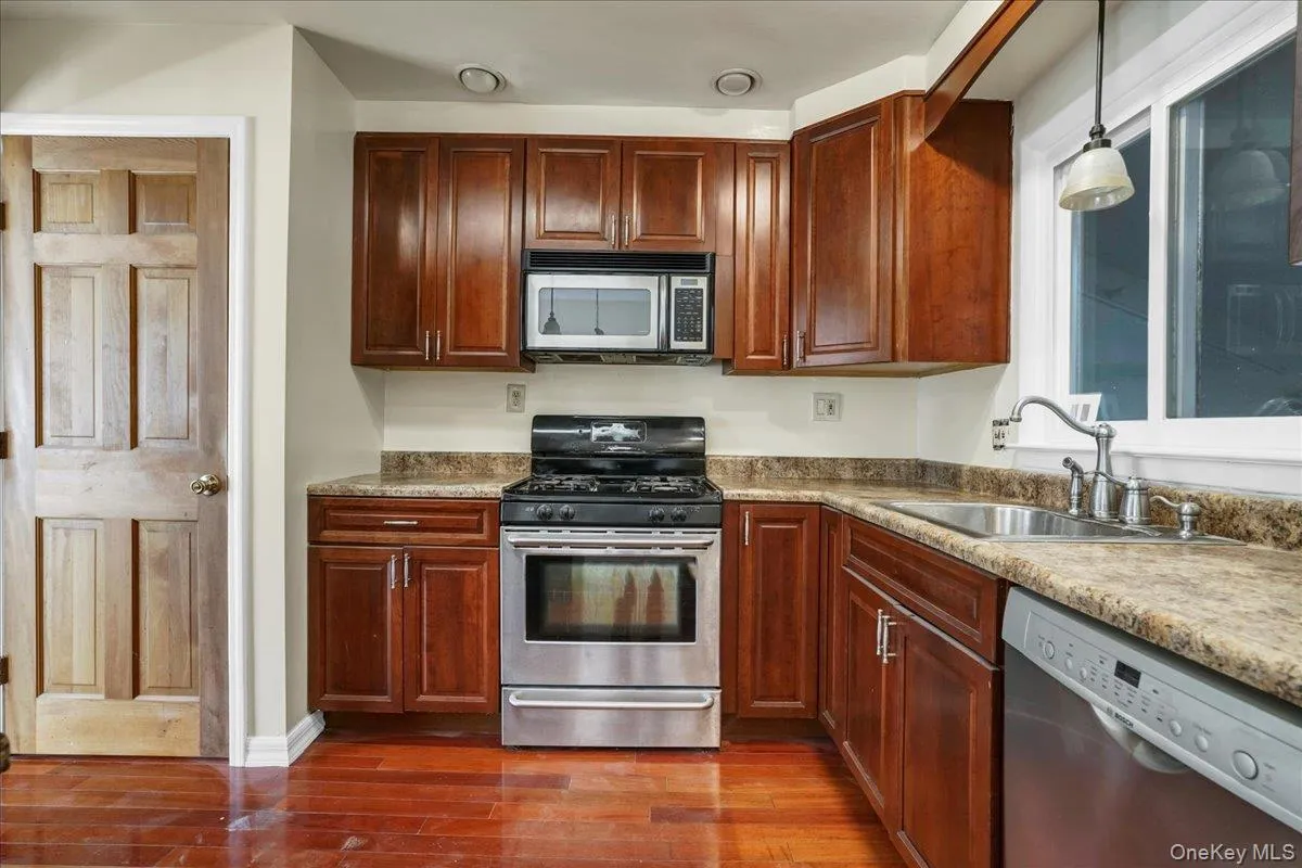 Kitchen featuring light stone counters, stainless steel appliances, dark wood-type flooring, sink, and hanging light fixtures Kitchen featuring light stone counters, stainless steel appliances, dark wood-type flooring, sink, and hanging light fixtures
