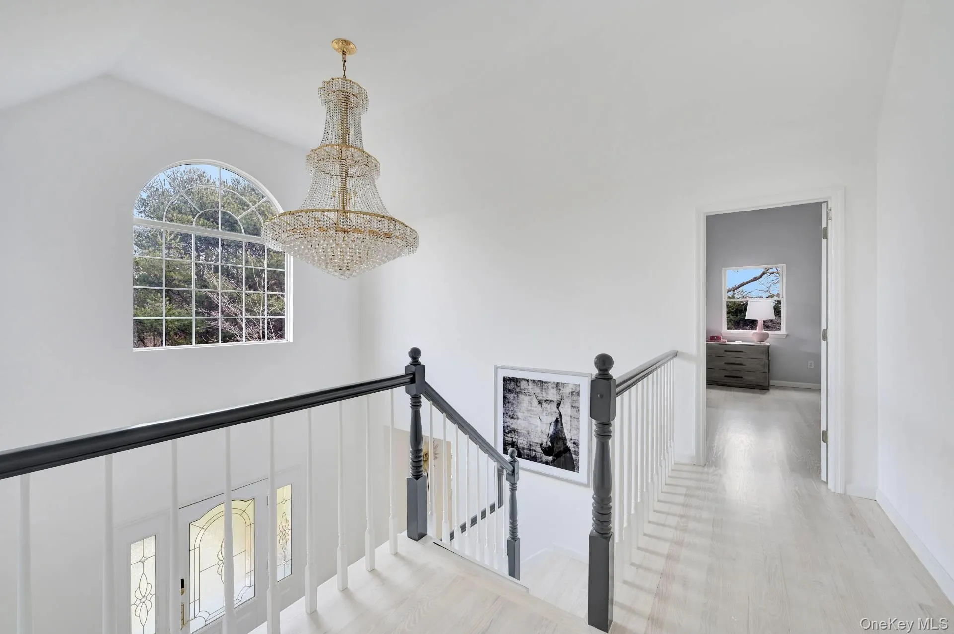 Hallway featuring an upstairs landing, light wood finished floors, vaulted ceiling, and a chandelier Hallway featuring an upstairs landing, light wood finished floors, vaulted ceiling, and a chandelier