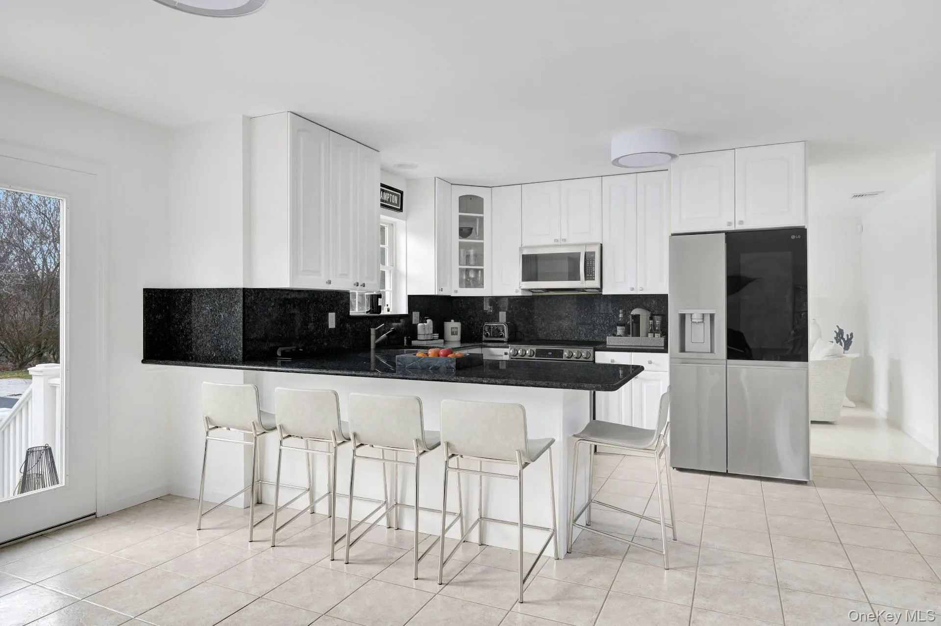 Kitchen with appliances with stainless steel finishes, tasteful backsplash, glass insert cabinets, a kitchen breakfast bar, and dark stone countertops Kitchen with appliances with stainless steel finishes, tasteful backsplash, glass insert cabinets, a kitchen breakfast bar, and dark stone countertops