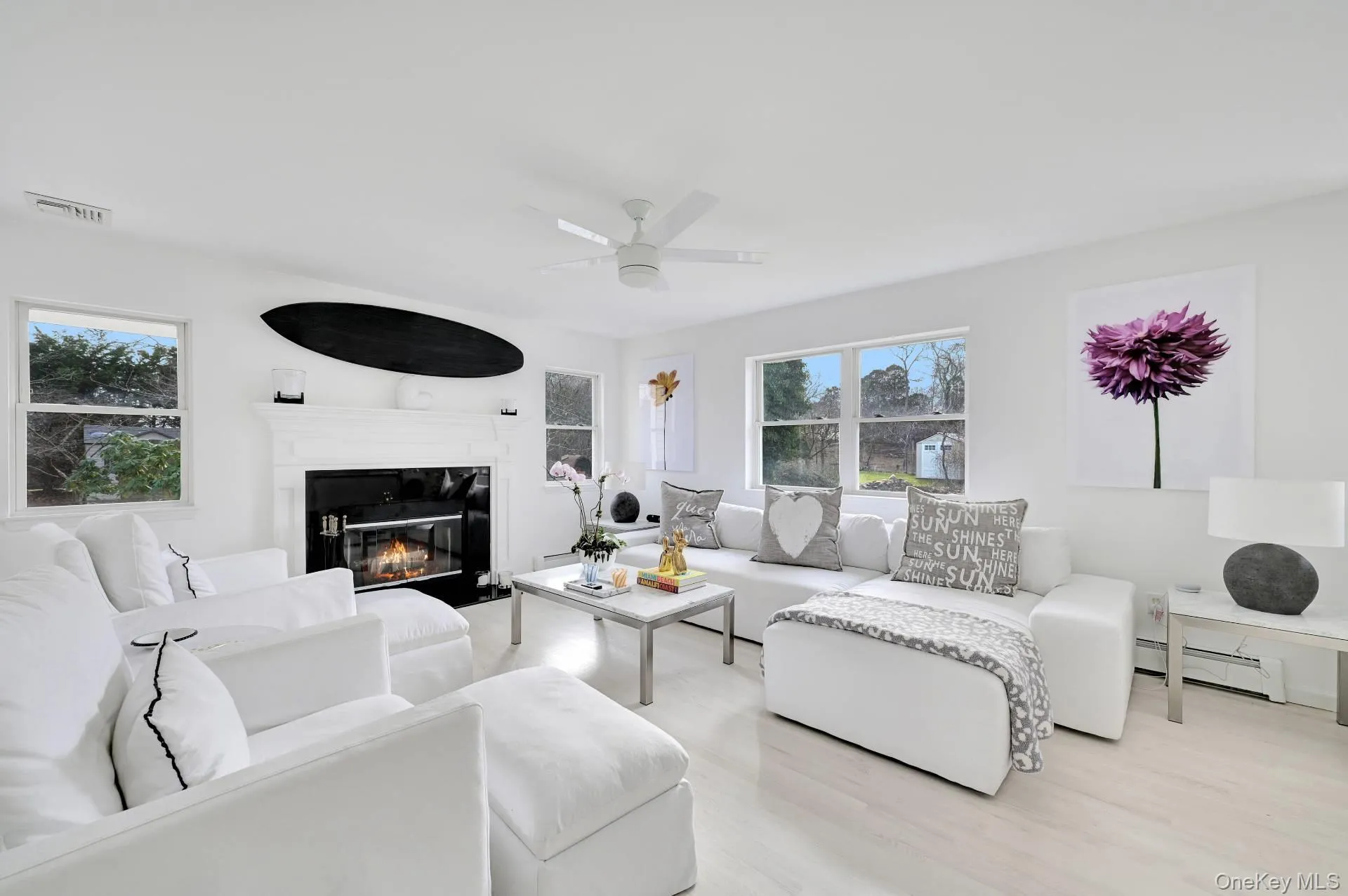 Living area featuring healthy amount of natural light, a baseboard radiator, wood finished floors, and a glass covered fireplace Living area featuring healthy amount of natural light, a baseboard radiator, wood finished floors, and a glass covered fireplace