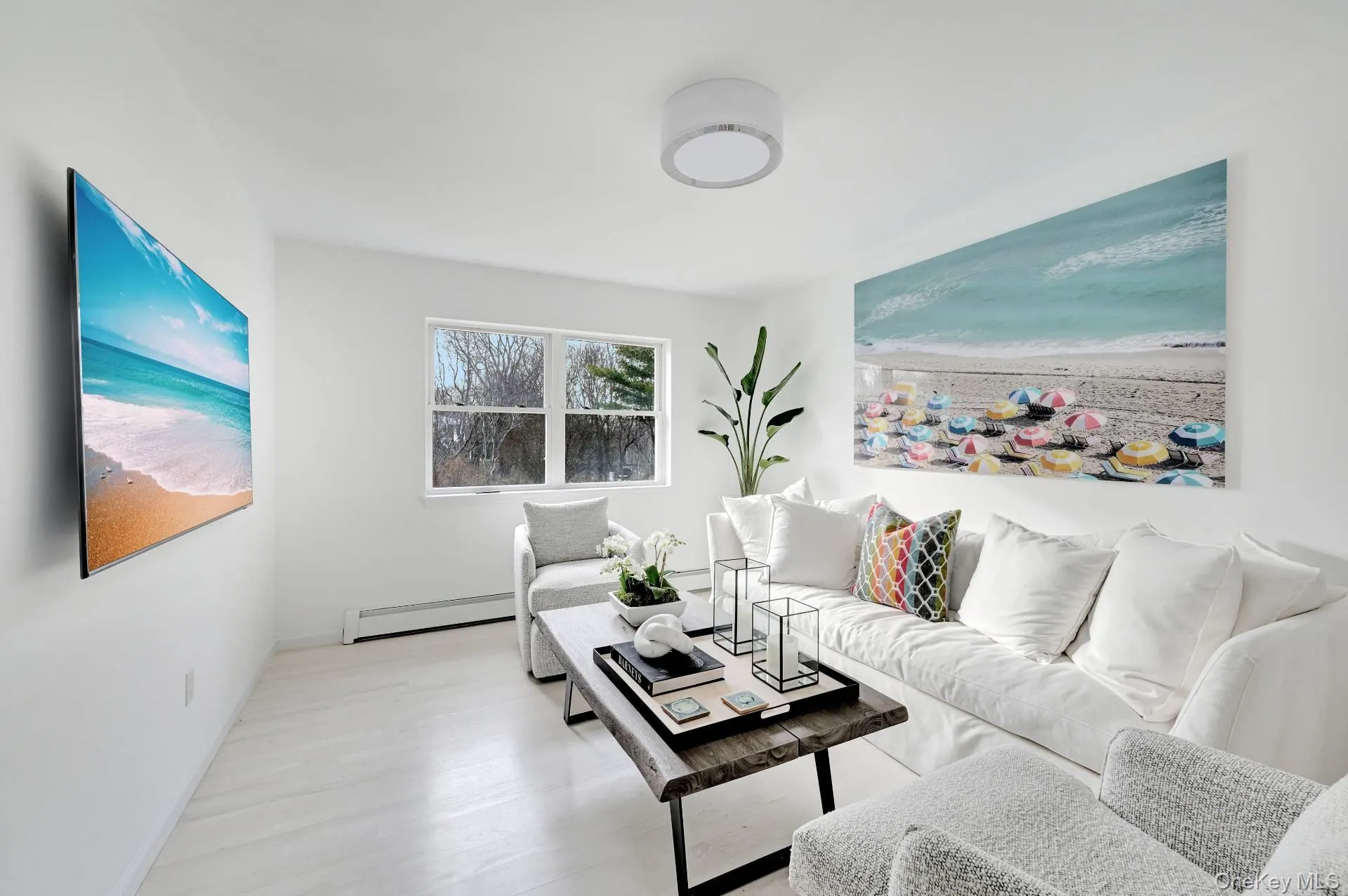 Living room with view of local beach, a baseboard heating unit, and light wood-style floors Living room with view of local beach, a baseboard heating unit, and light wood-style floors