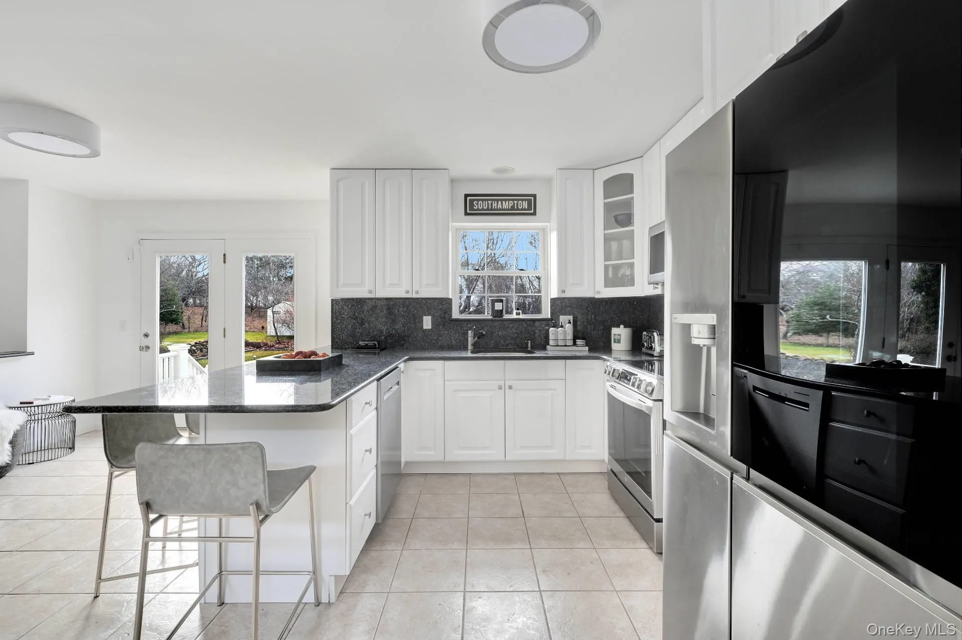 Kitchen featuring appliances with stainless steel finishes, a kitchen bar, a peninsula, decorative backsplash, and white cabinets Kitchen featuring appliances with stainless steel finishes, a kitchen bar, a peninsula, decorative backsplash, and white cabinets