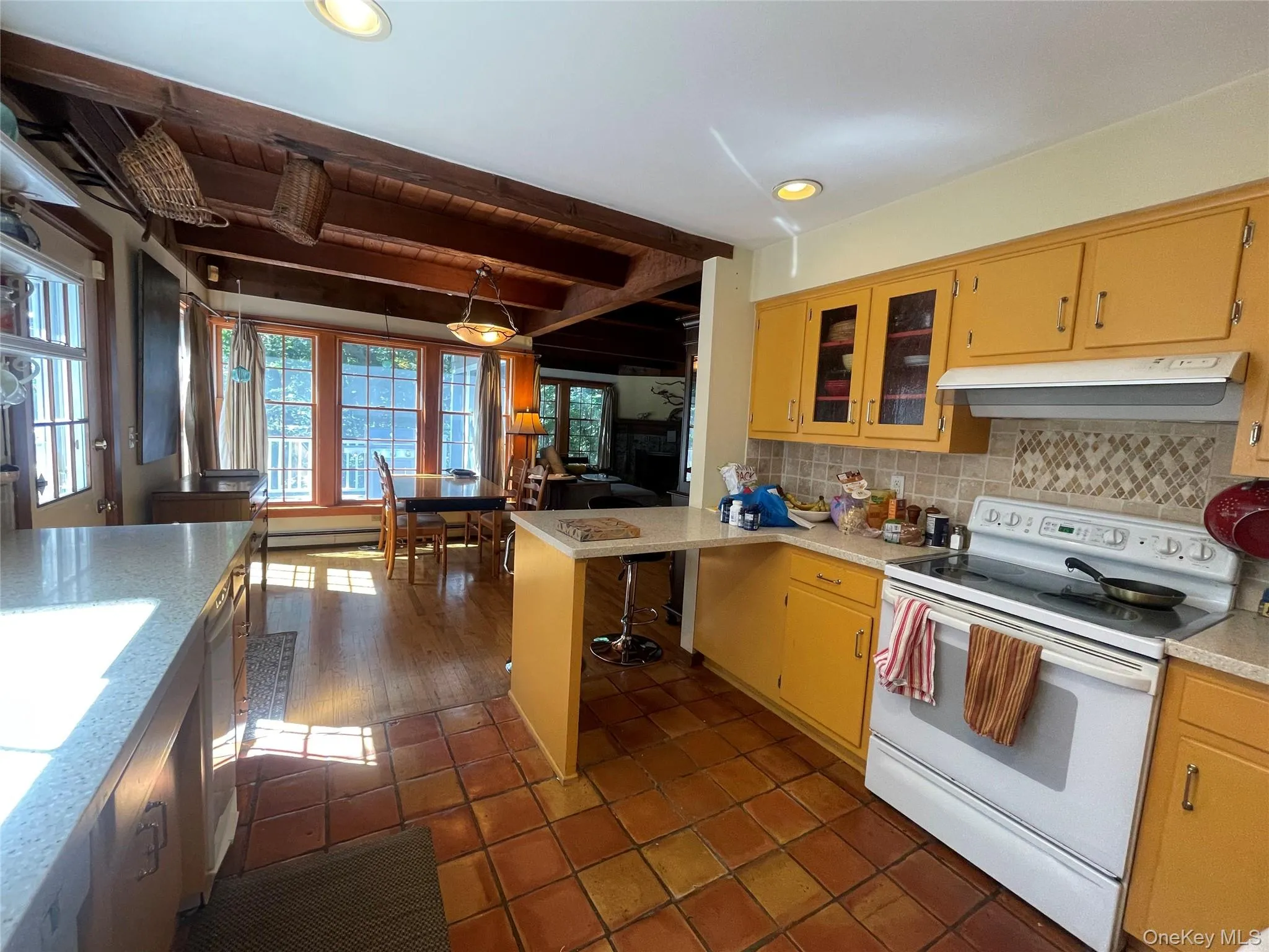 Kitchen featuring white range with electric stovetop, beam ceiling, decorative backsplash, light countertops, and hanging light fixtures Kitchen featuring white range with electric stovetop, beam ceiling, decorative backsplash, light countertops, and hanging light fixtures