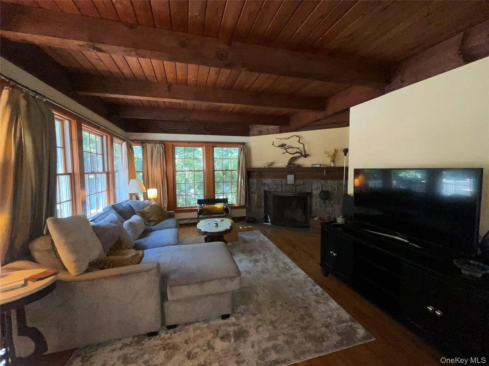 Living area with a stone fireplace, dark wood-style flooring, and a wooden ceiling with exposed beams Living area with a stone fireplace, dark wood-style flooring, and a wooden ceiling with exposed beams