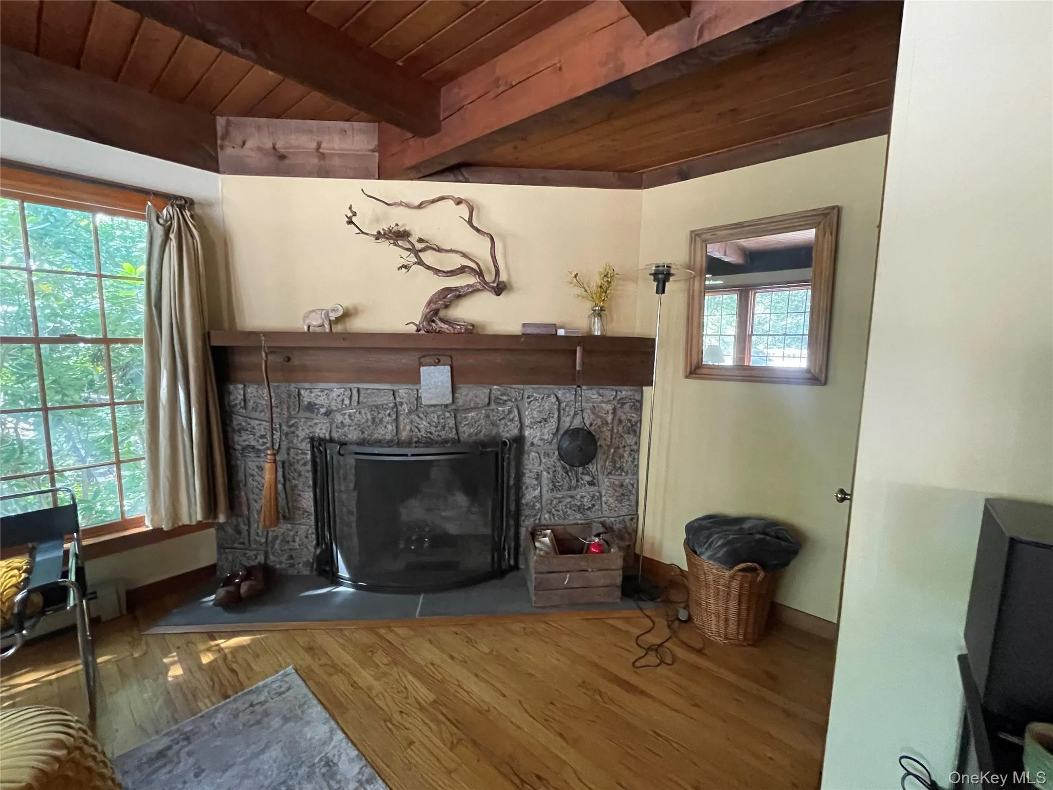 Living area featuring a wood ceiling with exposed beams, a stone fireplace, and wood finished floors Living area featuring a wood ceiling with exposed beams, a stone fireplace, and wood finished floors