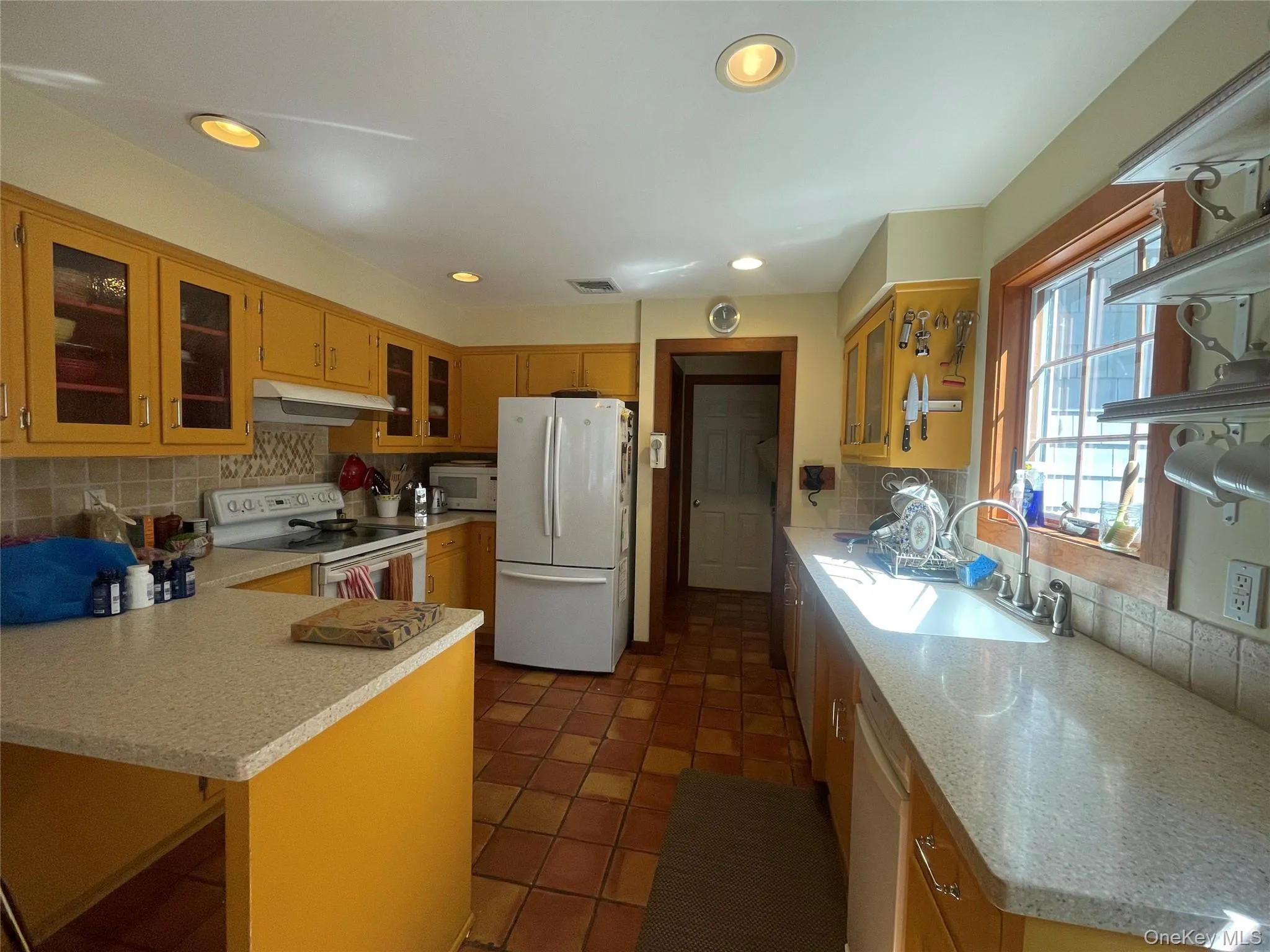 Kitchen with glass insert cabinets, decorative backsplash, white appliances, recessed lighting, and dark tile patterned floors Kitchen with glass insert cabinets, decorative backsplash, white appliances, recessed lighting, and dark tile patterned floors