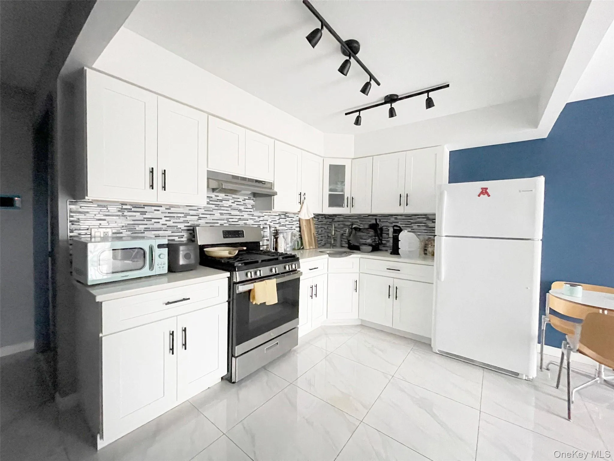 Kitchen with white cabinetry, white appliances, tasteful backsplash, and light countertops Kitchen with white cabinetry, white appliances, tasteful backsplash, and light countertops