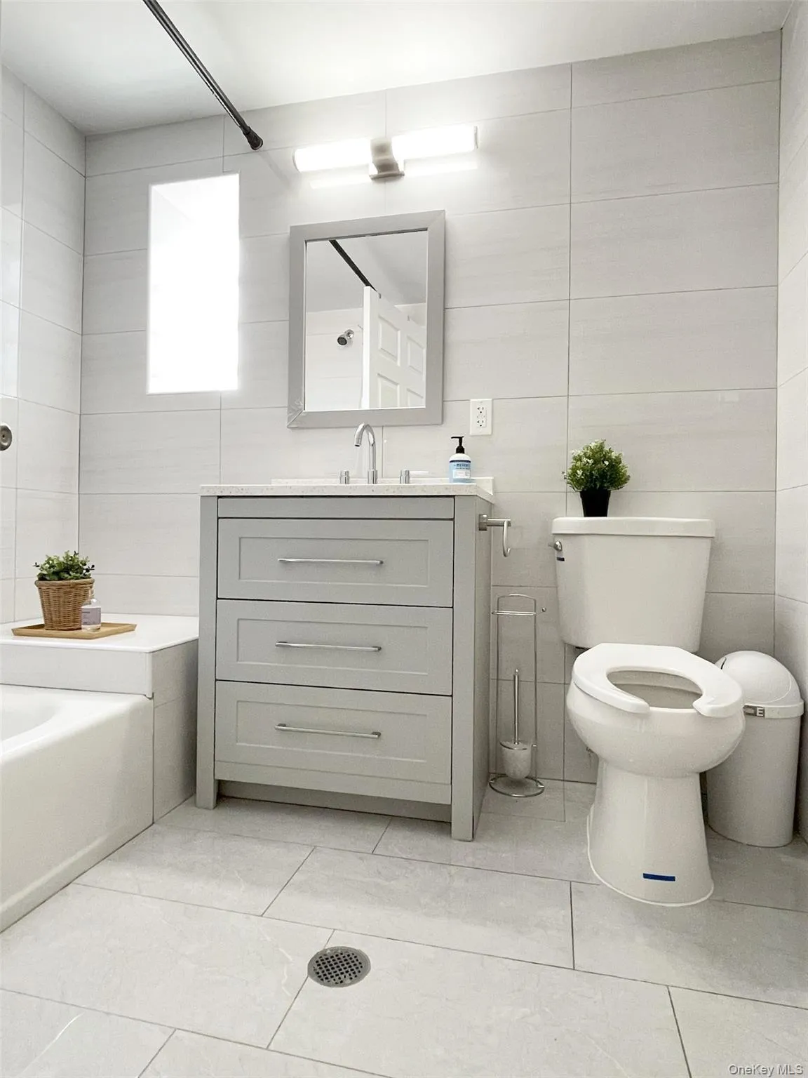 Full bath with tile walls, vanity, light tile patterned floors, and washtub / shower combination Full bath with tile walls, vanity, light tile patterned floors, and washtub / shower combination