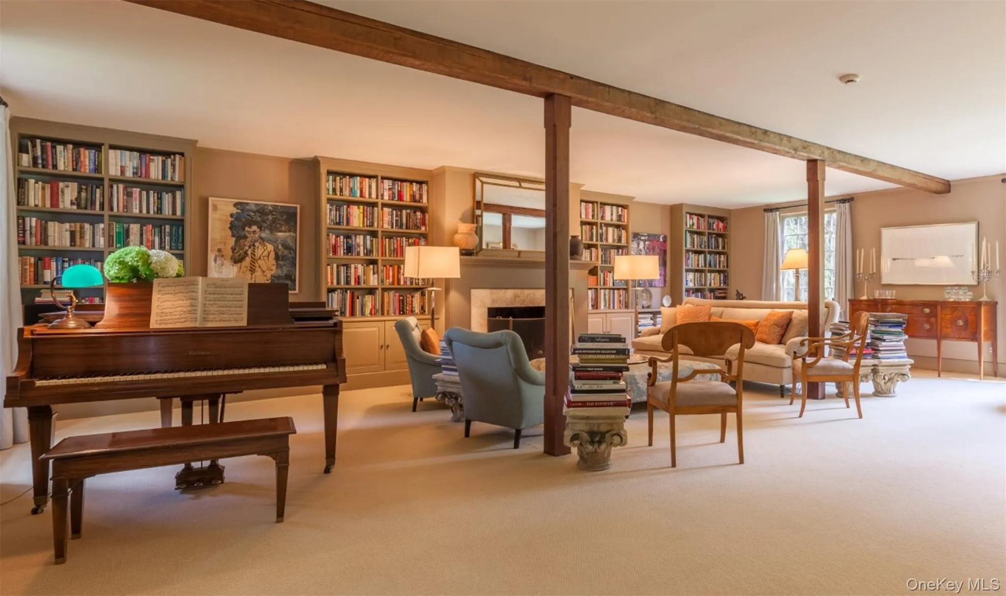 Living area with beam ceiling, a fireplace, carpet floors, and bookshelves Living area with beam ceiling, a fireplace, carpet floors, and bookshelves