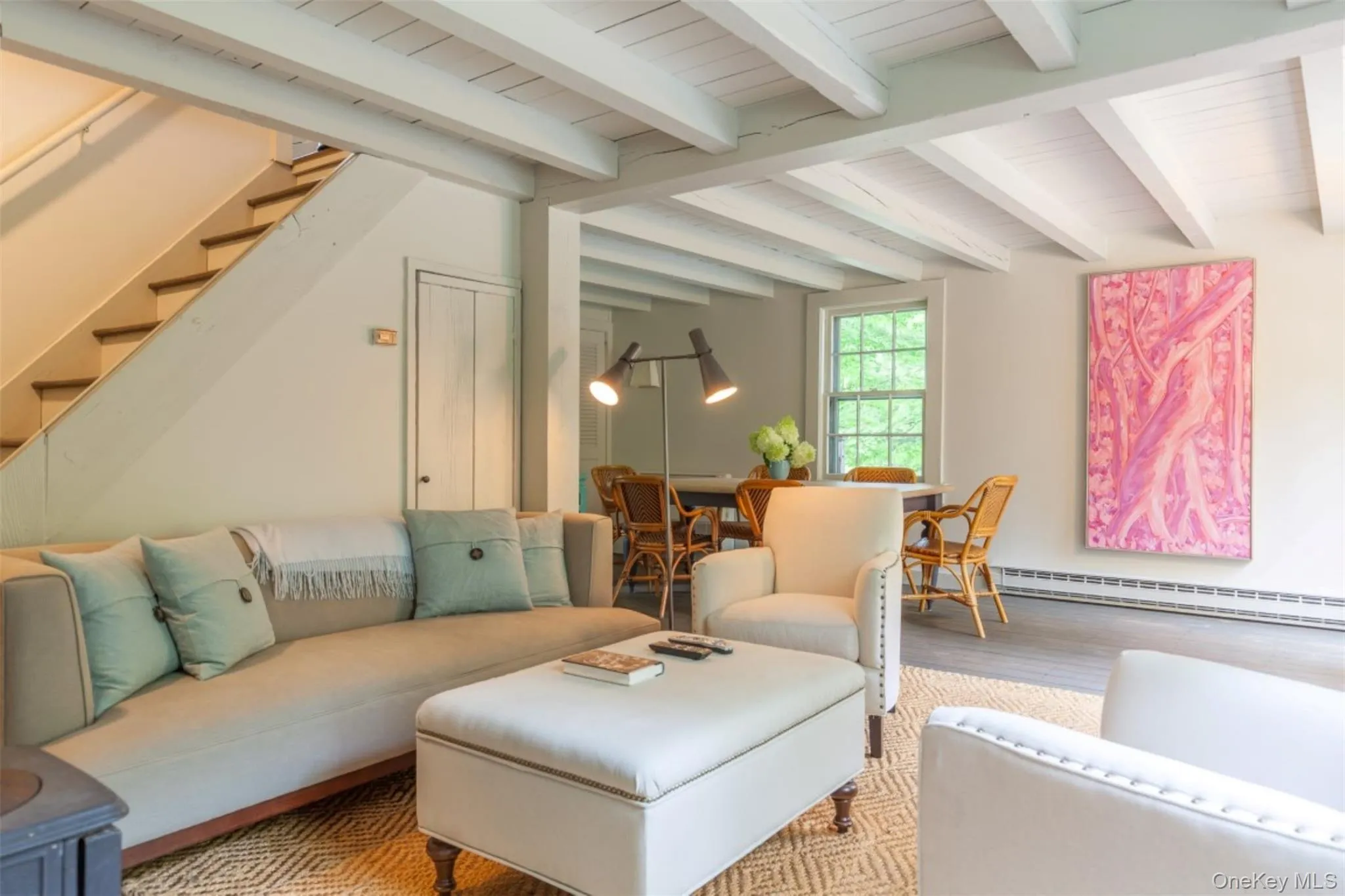 Living room featuring stairway, a baseboard heating unit, beamed ceiling, and wood finished floors Living room featuring stairway, a baseboard heating unit, beamed ceiling, and wood finished floors