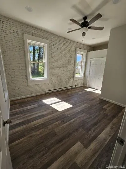 Unfurnished bedroom with dark wood-style floors, brick wall, a baseboard radiator, a ceiling fan, and a closet Unfurnished bedroom with dark wood-style floors, brick wall, a baseboard radiator, a ceiling fan, and a closet
