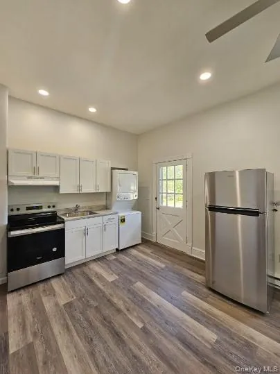 Kitchen featuring stainless steel appliances, white cabinets, recessed lighting, stacked washer and clothes dryer, and dark wood-style floors Kitchen featuring stainless steel appliances, white cabinets, recessed lighting, stacked washer and clothes dryer, and dark wood-style floors