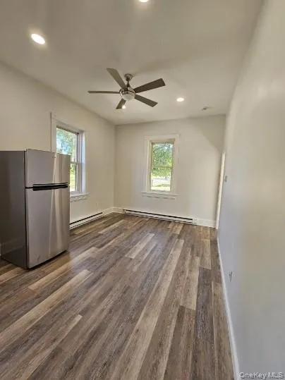Empty room with plenty of natural light, recessed lighting, dark wood-style floors, and a baseboard radiator Empty room with plenty of natural light, recessed lighting, dark wood-style floors, and a baseboard radiator
