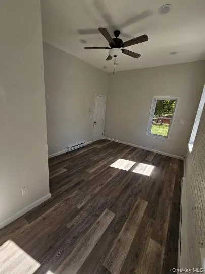 Empty room featuring dark wood-type flooring, ceiling fan, and a baseboard heating unit Empty room featuring dark wood-type flooring, ceiling fan, and a baseboard heating unit