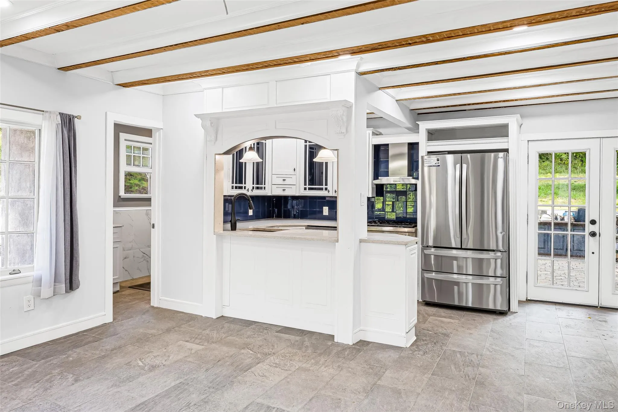 Kitchen featuring freestanding refrigerator, beamed ceiling, decorative backsplash, white cabinetry, and range hood Kitchen featuring freestanding refrigerator, beamed ceiling, decorative backsplash, white cabinetry, and range hood
