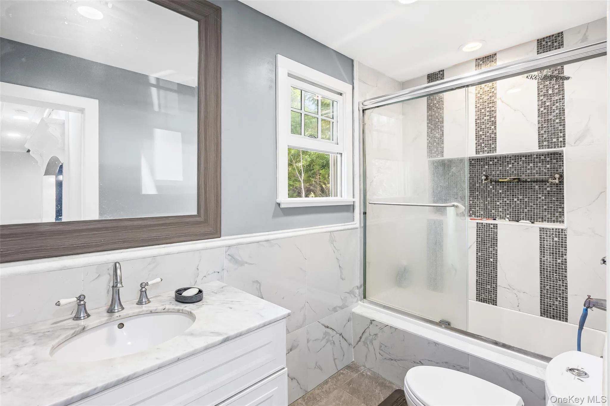 Bathroom with vanity, tile walls, shower / bath combination with glass door, recessed lighting, and a wainscoted wall Bathroom with vanity, tile walls, shower / bath combination with glass door, recessed lighting, and a wainscoted wall